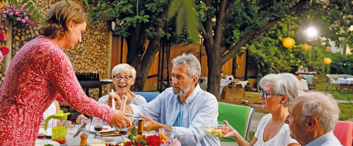 Woman hosting a dinner party and serving salad to friends around the dining table